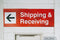 Red shipping and receiving sign with white text and green arrow pointing left on a white wall.